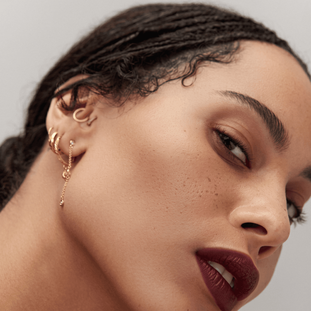Mixed gold hoops, floral studs, and an arrow earring styled with the eclectic ear piercing aesthetic of Zoë Kravitz